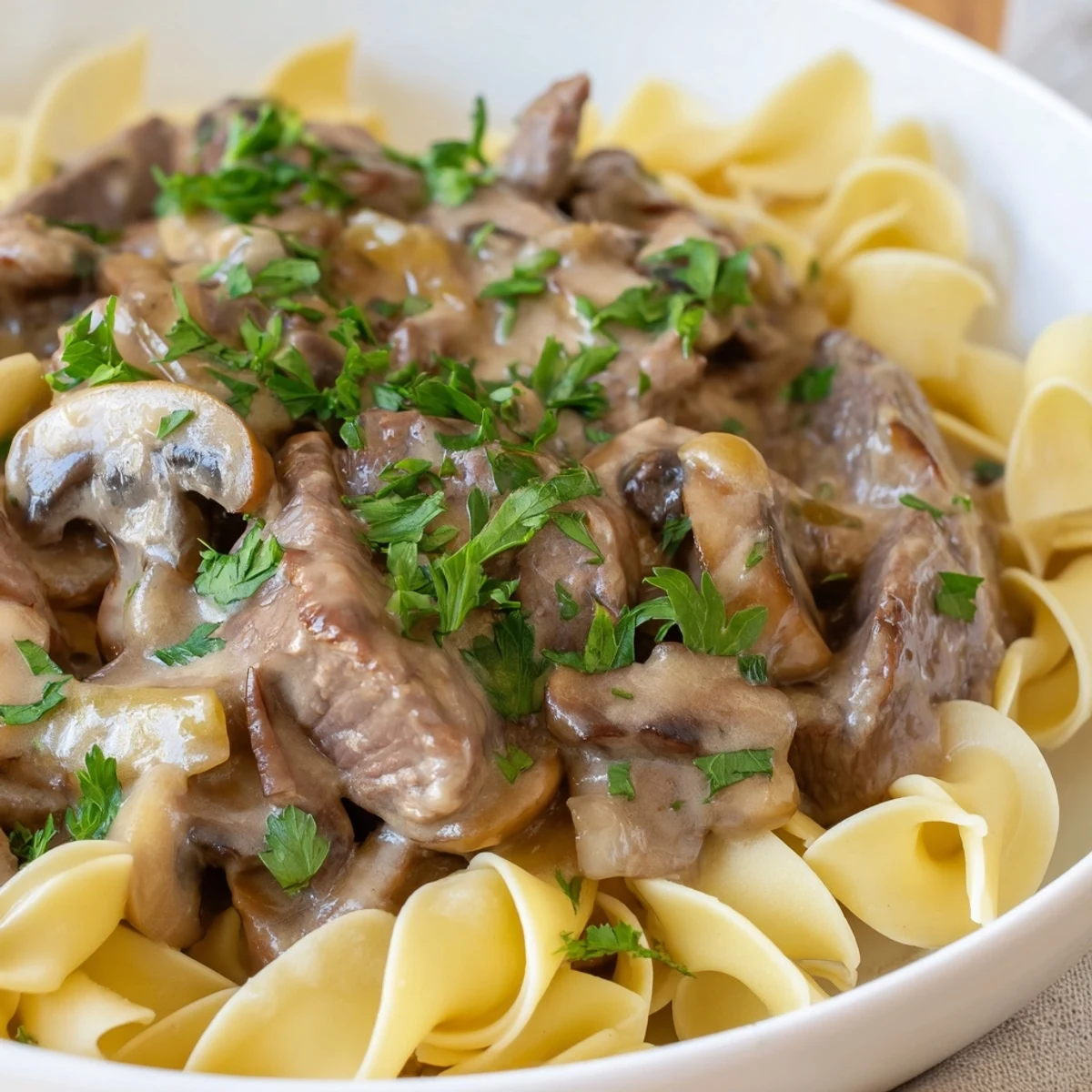 Creamy Beef Stroganoff with Mushroom Gravy spooned over tender egg noodles, garnished with fresh parsley.