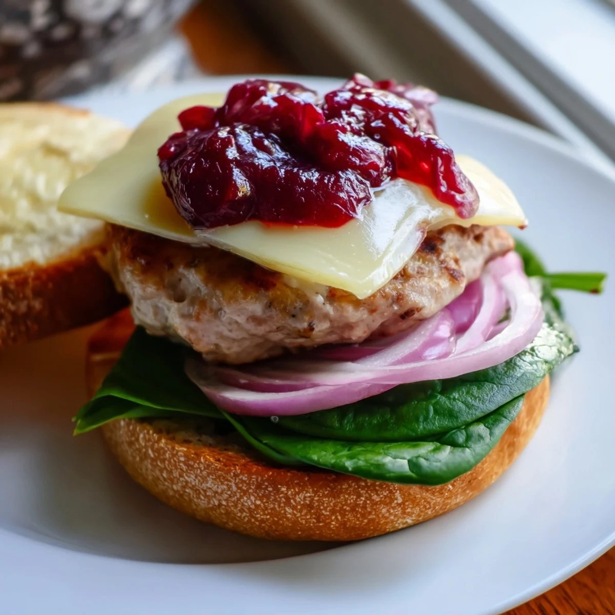 Juicy turkey burgers with cranberry sauce and Brie, cheese melting over the patty on a toasted bun with spinach.