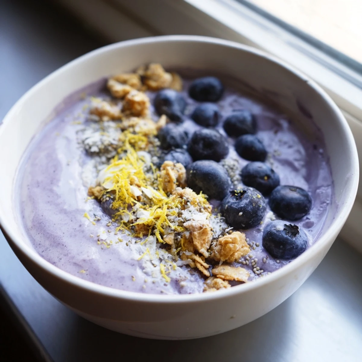 Thick and creamy Lemon Blueberry Smoothie Bowl with chia seeds and coconut flakes in a white ceramic bowl.