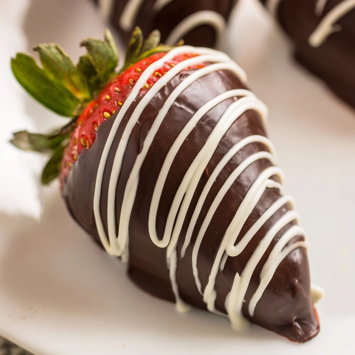 Close-up of chocolate dipped strawberries with white drizzle served on a plate, ready for a party.