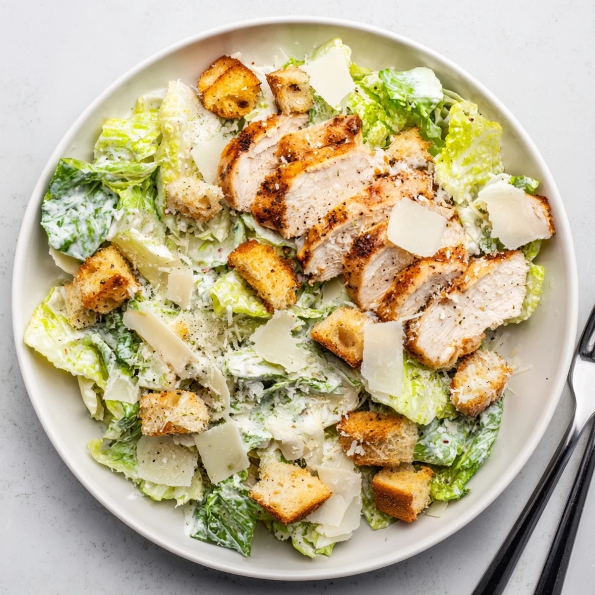 A close-up of a freshly tossed Chicken Caesar Salad highlights creamy dressing coating each leaf, with savory grilled chicken and golden-brown croutons adding texture and flavor.