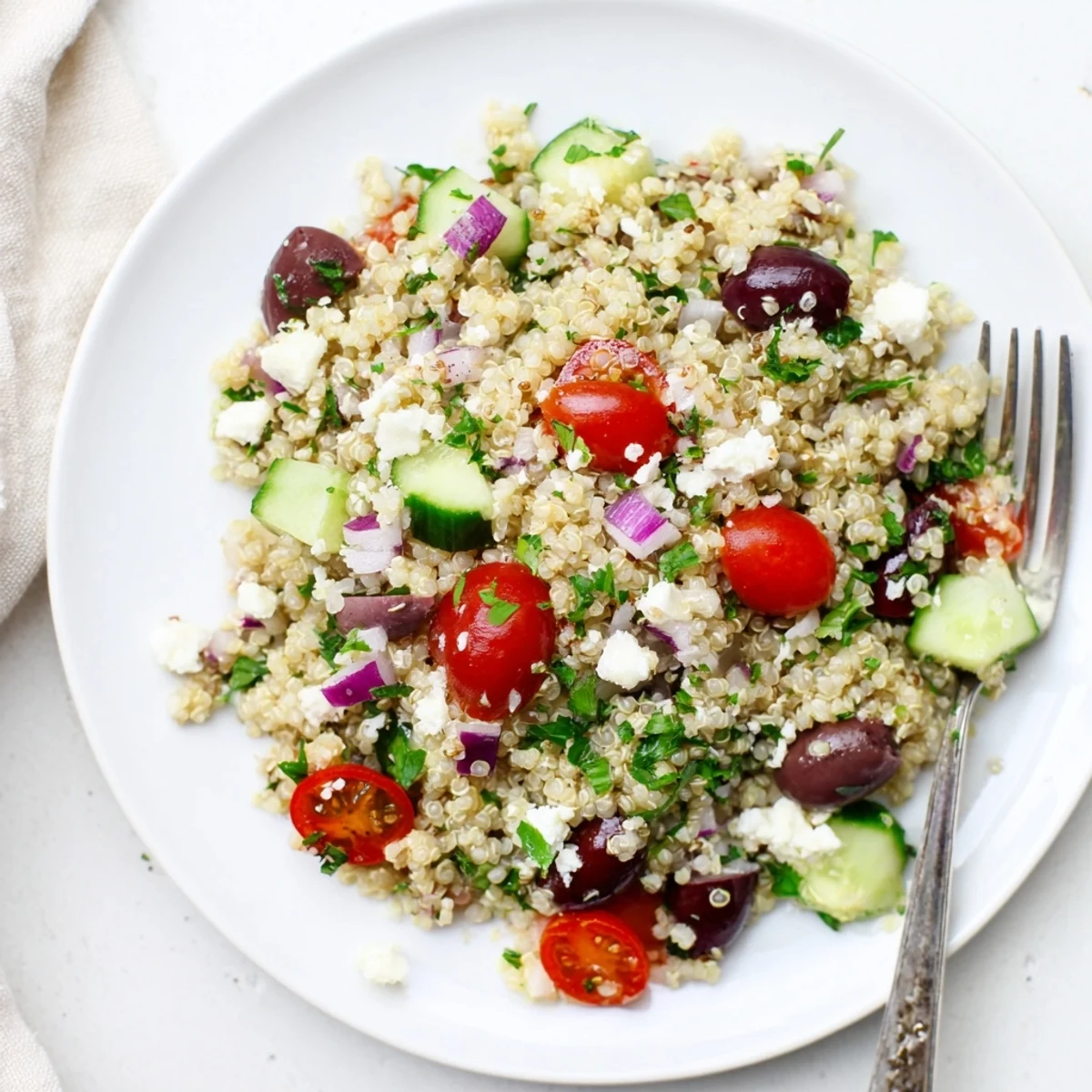 Fluffy quinoa salad with tomatoes, cucumbers, and feta on a white plate.