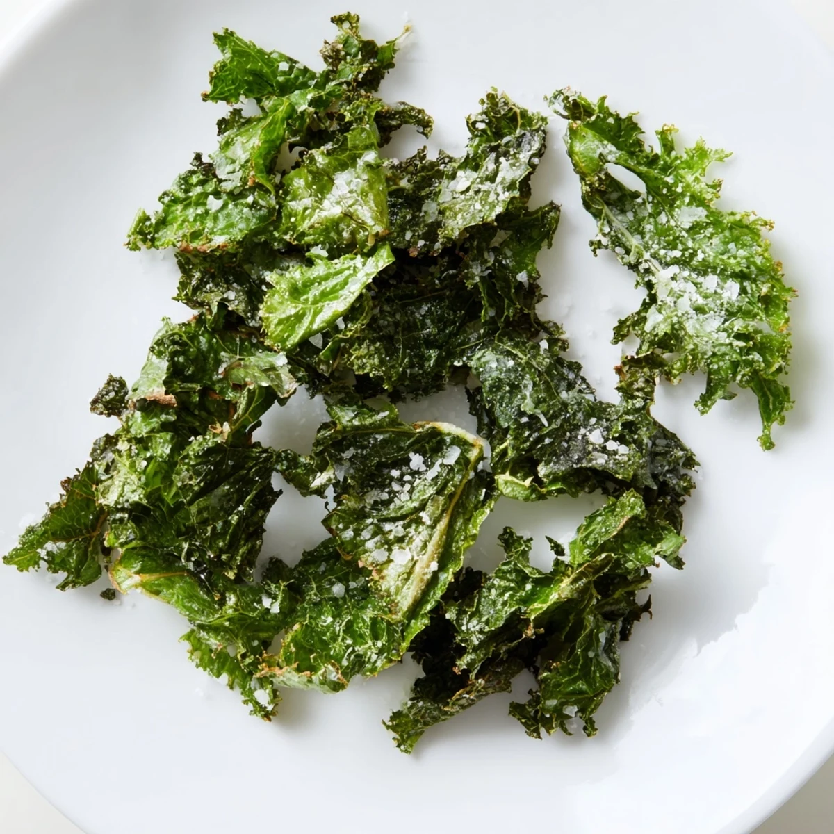 Vibrant green kale chips with sea salt, lightly crisped edges, perfect for dipping in a creamy sauce.