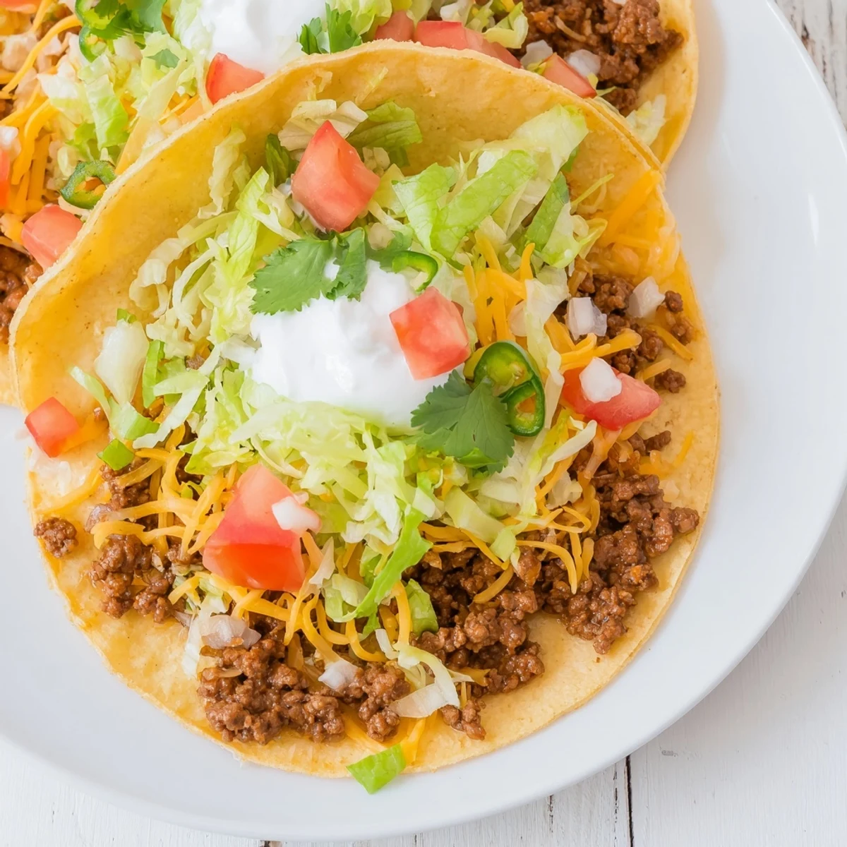 A close-up of MVP Beef Tacos with cheese and sour cream drizzled over shredded lettuce and diced tomatoes.  