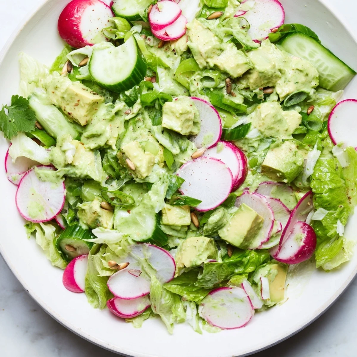 Freshly chopped romaine lettuce topped with creamy diced avocado, crisp cucumber slices, and vibrant radishes. Tossed with a vibrant homemade green goddess dressing and a sprinkle of toasted sunflower seeds. This refreshing bowl is served on a rustic wooden table, perfect for a light lunch.