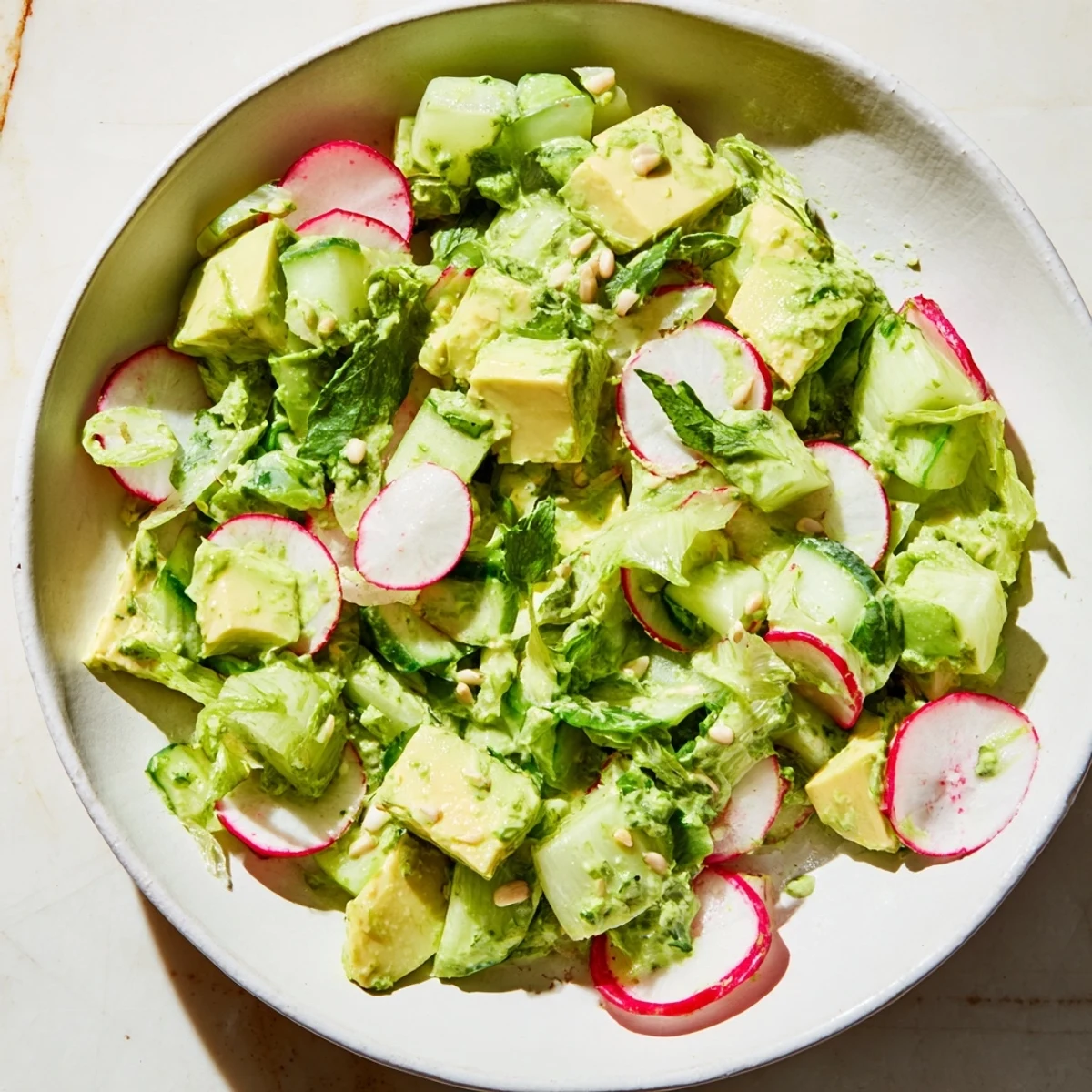 A close-up of a vibrant green goddess salad featuring ripe avocado chunks, sliced radishes, and scallions. The salad is tossed in a creamy, herbaceous dressing, garnished with fresh parsley and tarragon. Perfectly plated for a summer potluck or a quick gluten-free dinner.