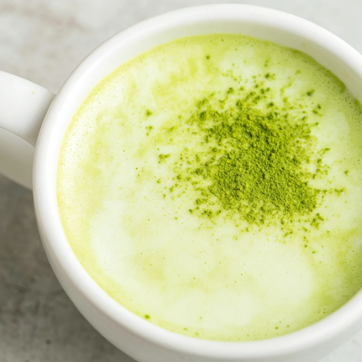 The bright green hue of this Green Matcha Latte with Oat Milk contrasts beautifully against a clean, minimalist kitchen backdrop.