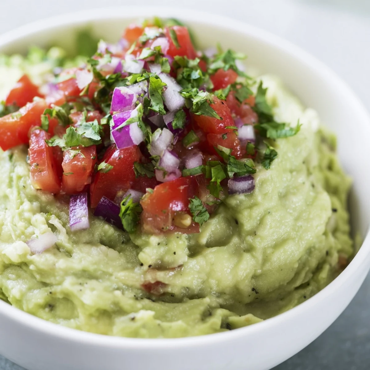 Creamy avocado guacamole with fresh pico de gallo garnished with lime wedges and cilantro, a perfect vegetarian appetizer for game day parties.  