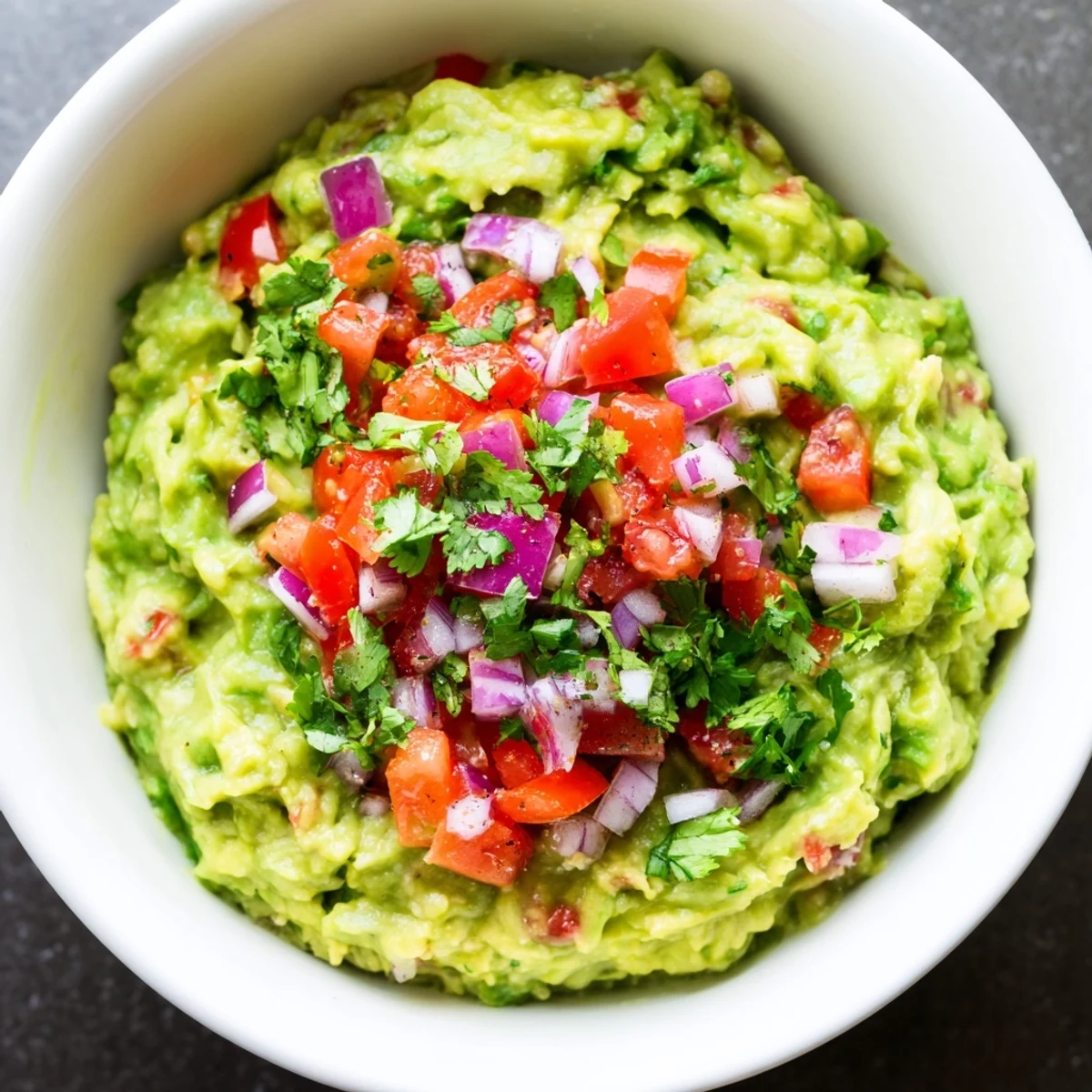 Bright bowl of guacamole with fresh pico de gallo featuring juicy tomatoes and jalapeños, ready to scoop with crunchy tortilla chips at a gathering.