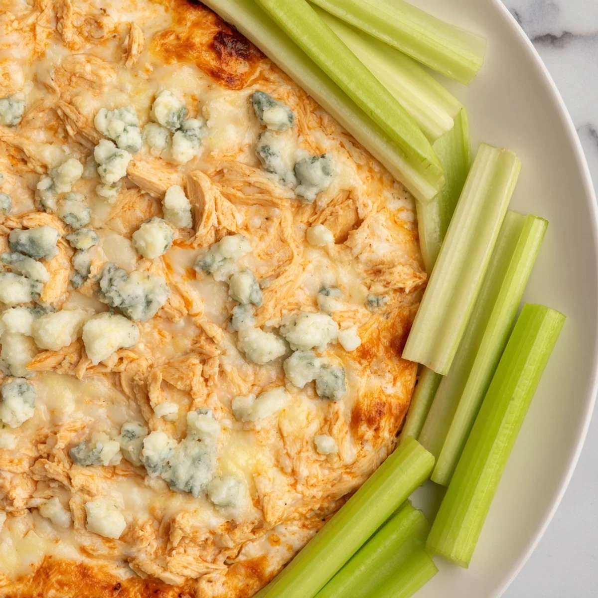 A warm bowl of Spicy Buffalo Chicken Dip with celery sticks on a rustic table, steam rising from the melted cheese.