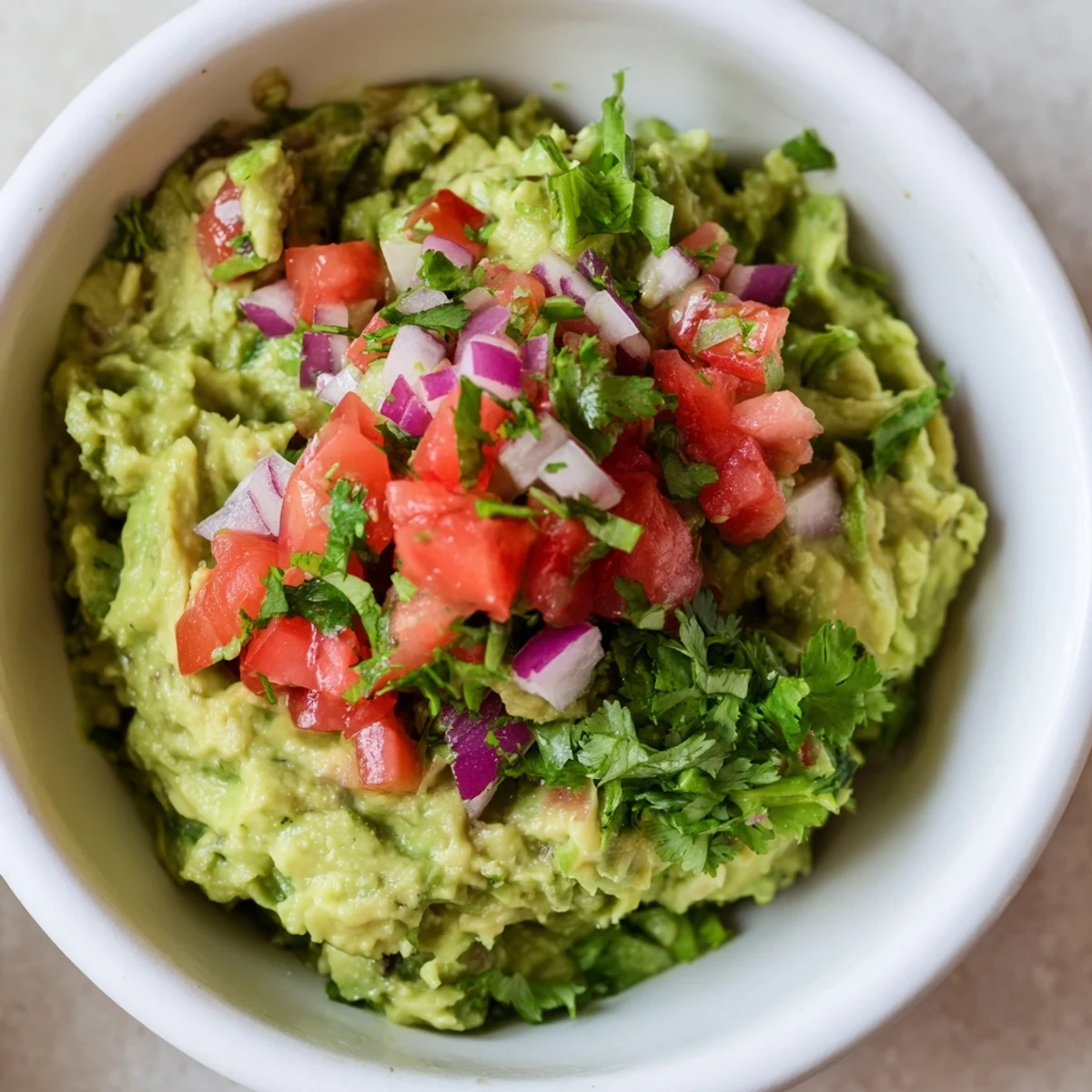 A vibrant bowl of guacamole with fresh pico de gallo and lime, garnished with red onion, perfect as a taco topping.