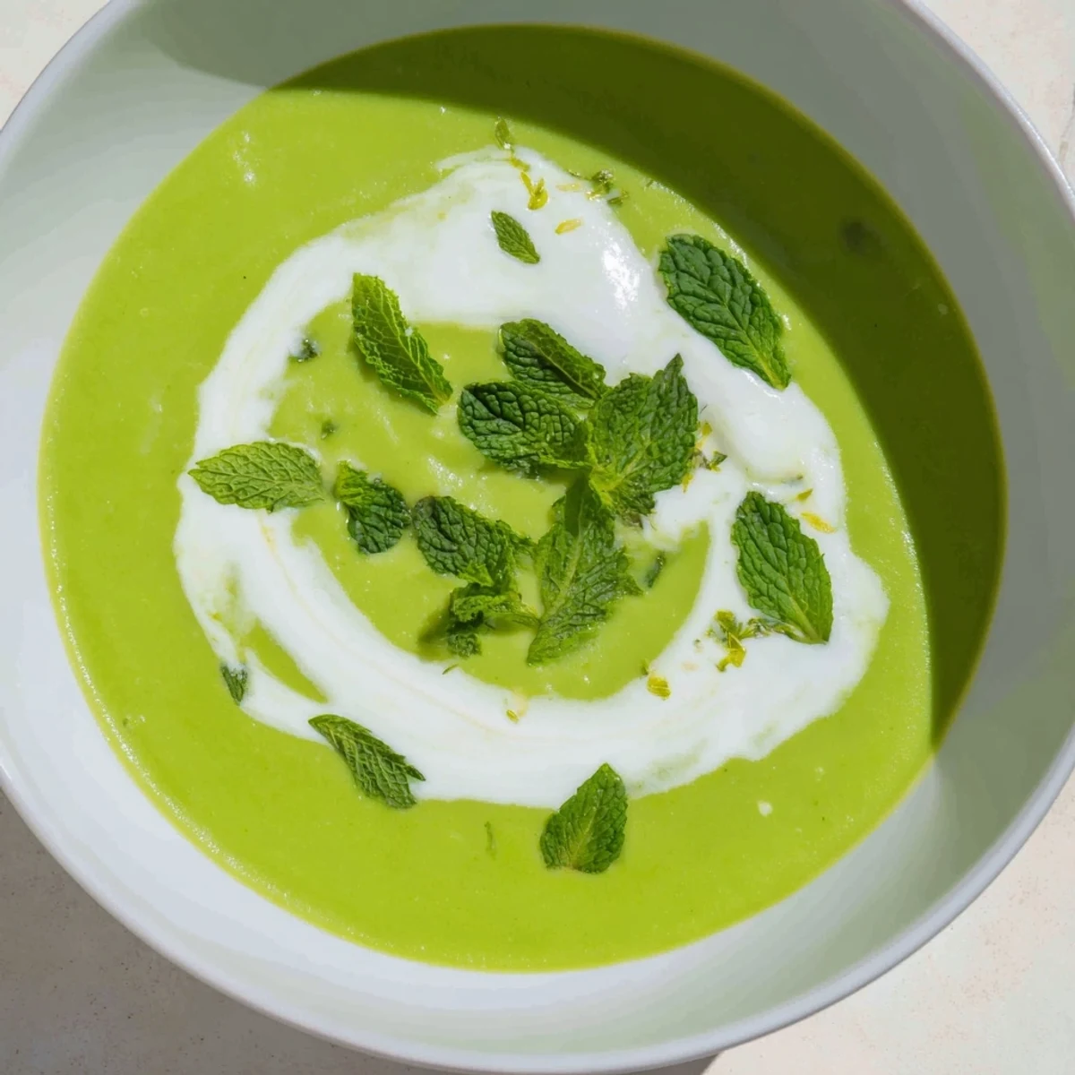 A bowl of vibrant Spring Pea Soup with Mint and Crème Fraîche garnished with fresh mint and a lemon zest swirl.