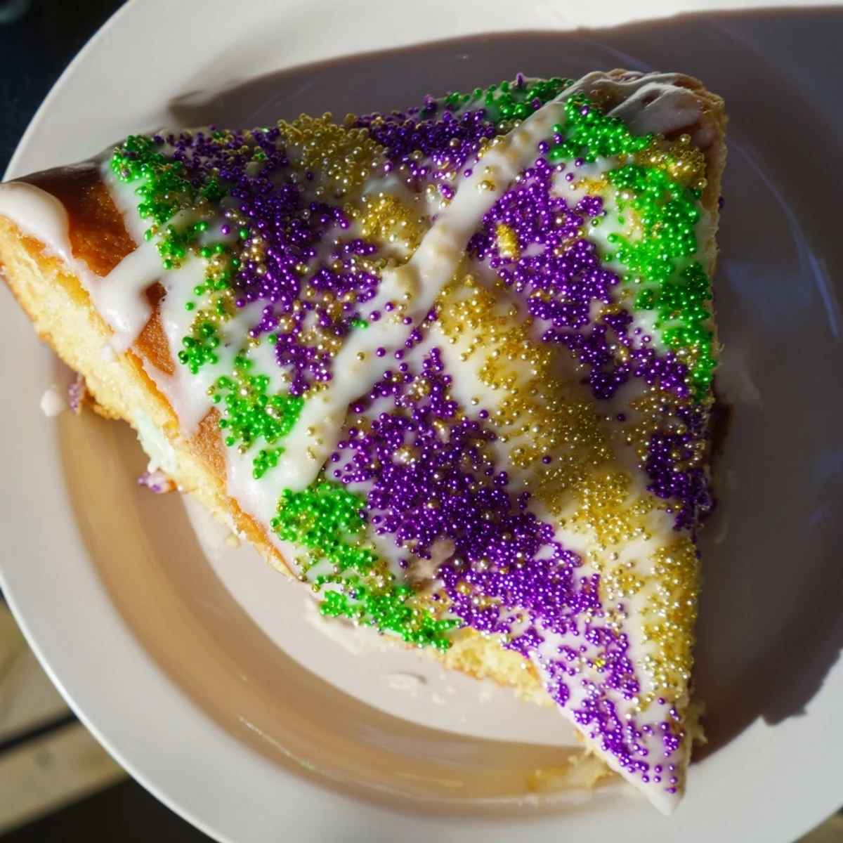A sliced Mardi Gras Style King Cake reveals creamy filling, dusted with colorful sugars on a festive plate.