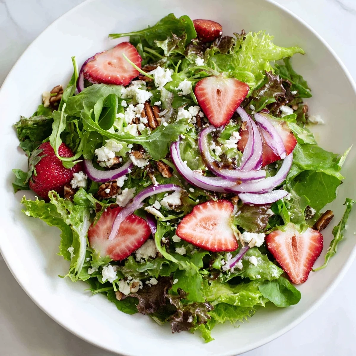 The Spring Greens Salad with Strawberries and Goat Cheese is tossed in a light balsamic vinaigrette, served in a ceramic bowl perfect for a healthy lunch.