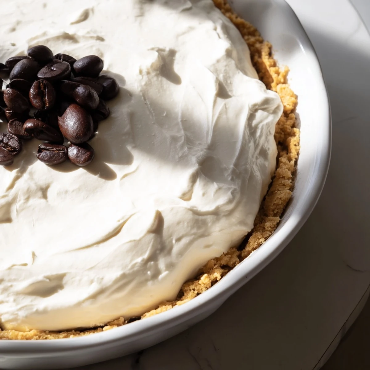 A smooth keto coffee dessert is shown in this Keto Cold Brew Coffee Pie with a light whipped topping and coffee bean garnish.