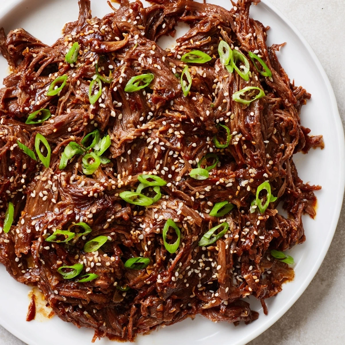 Tender Slow Cooker Korean Beef shredded and glistening with savory-sweet sauce, served over fluffy white rice with green onions.