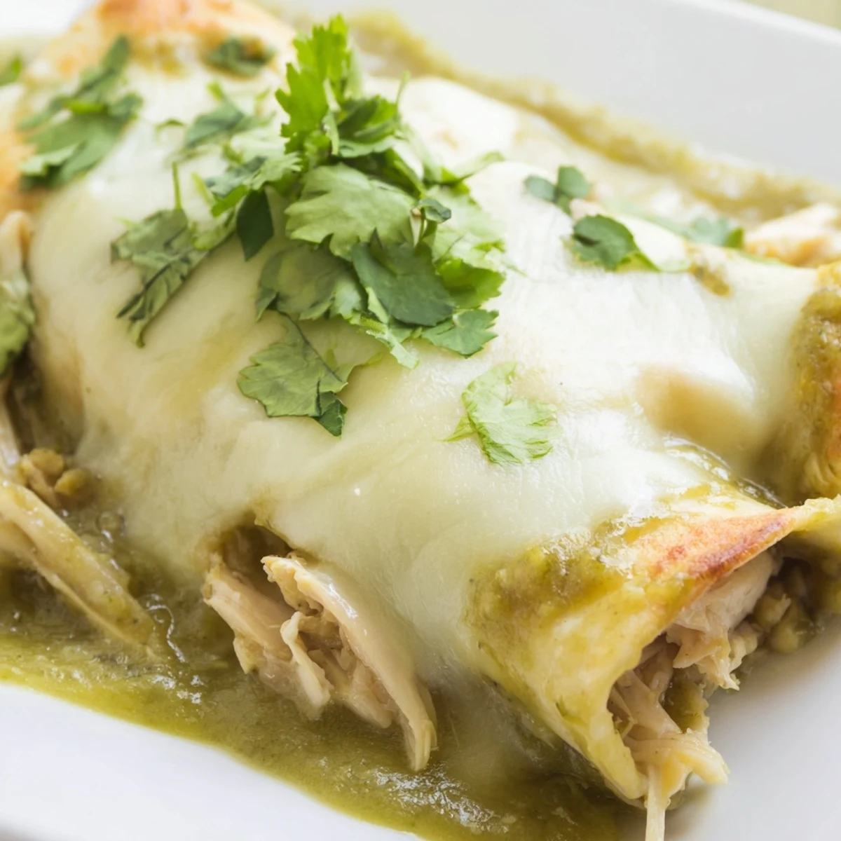 A casserole dish of Green Enchiladas With Chicken bubbles with melted Monterey Jack cheese for a comforting meal.