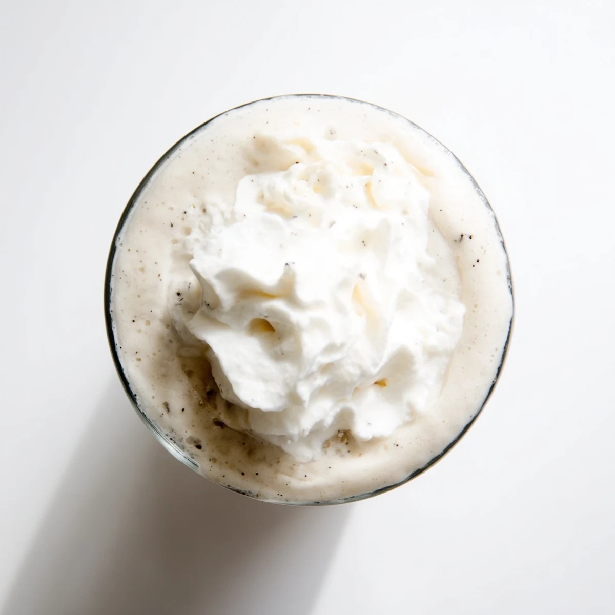 Creamy Starbucks Vanilla Bean Frappuccino topped with whipped cream in a tall glass, served with a straw on a sunny patio table.