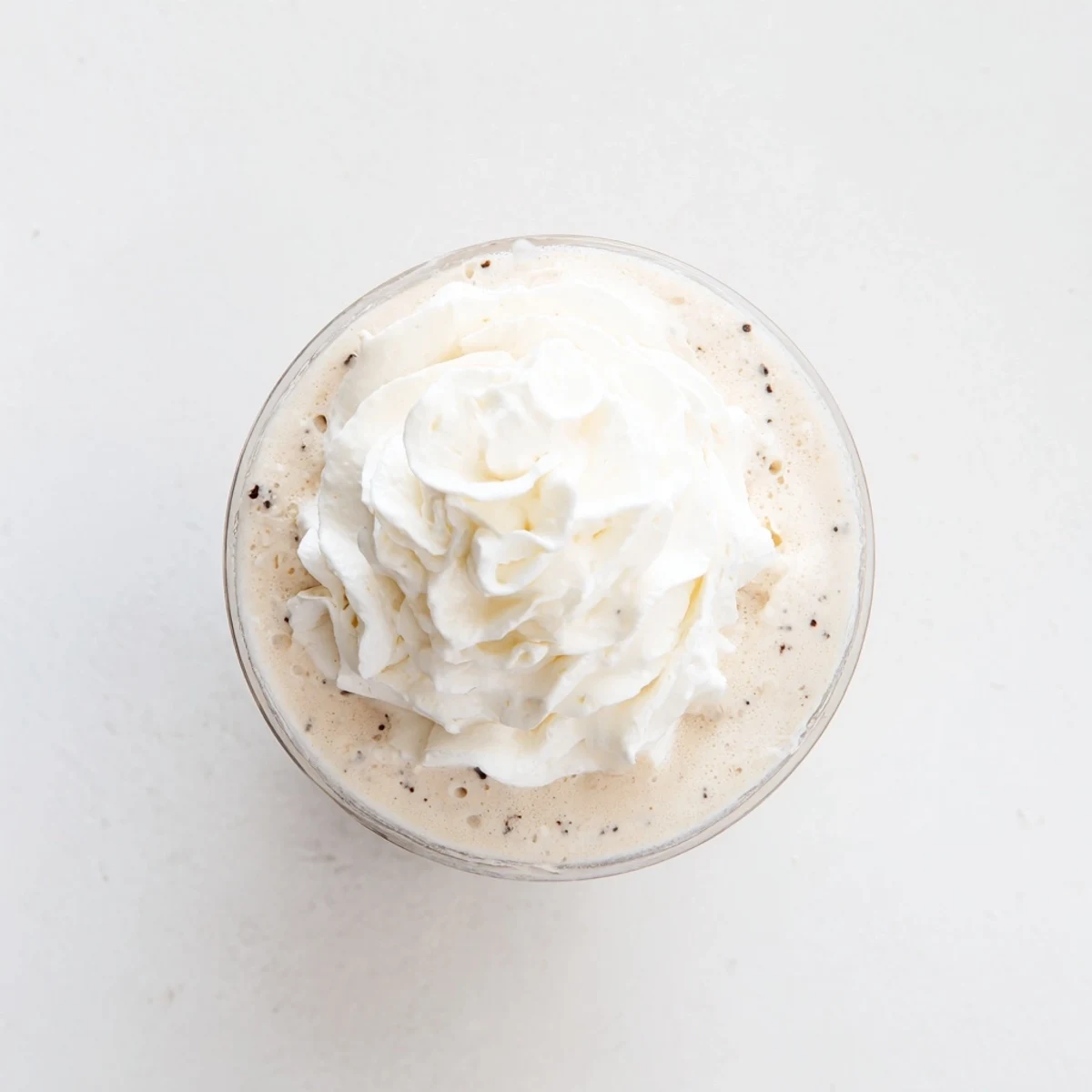 Frozen Starbucks Vanilla Bean Frappuccino with vanilla bean specks, next to whole beans and fresh whipped cream topping.