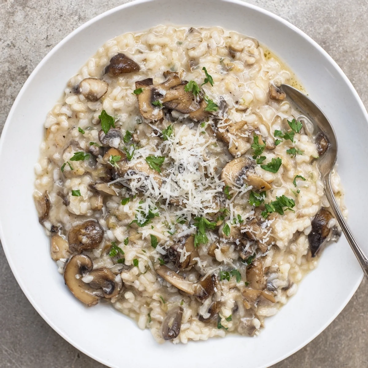 A spoon lifts a creamy serving of Creamy Mushroom Risotto, revealing its rich texture and sautéed mushroom pieces.
