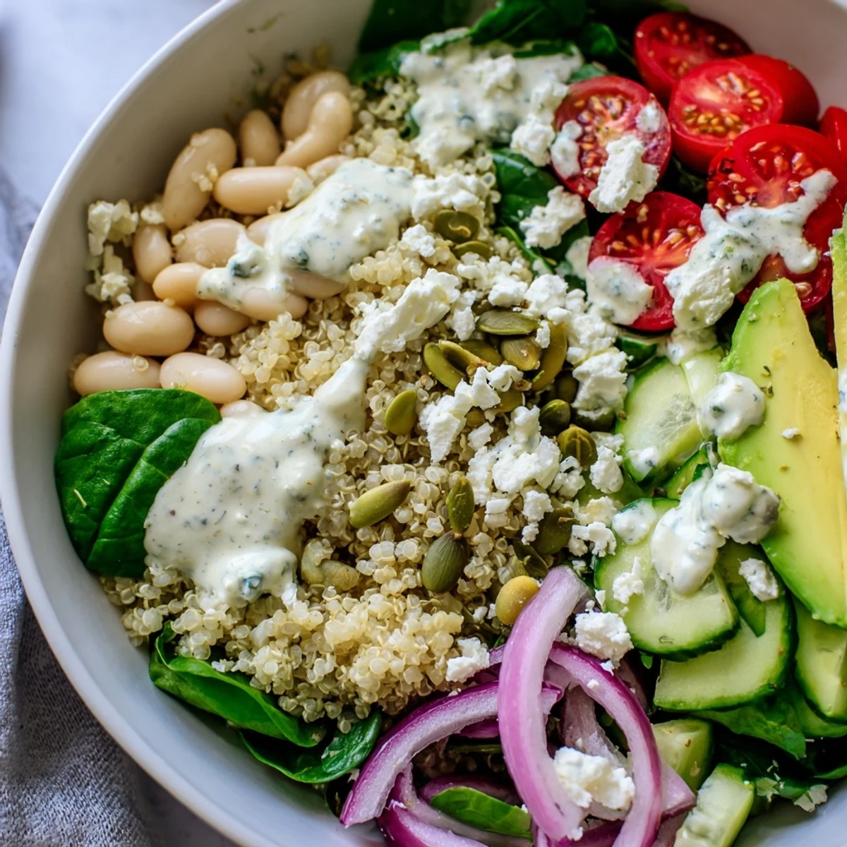 Bright lemon-tahini dressing drizzles over the Spinach & White Bean Ultimate Protein Power Bowl, topped with pumpkin seeds and feta.