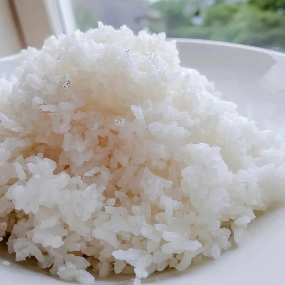 Fluffy The Best Coconut Rice in a white bowl, garnished with toasted coconut flakes and a lime wedge.