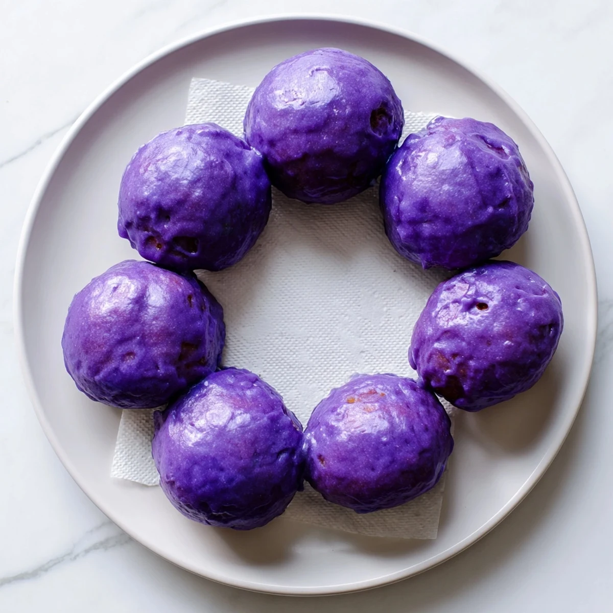 Freshly fried Ube Mochi Donuts with a vibrant purple glaze on a wire rack.