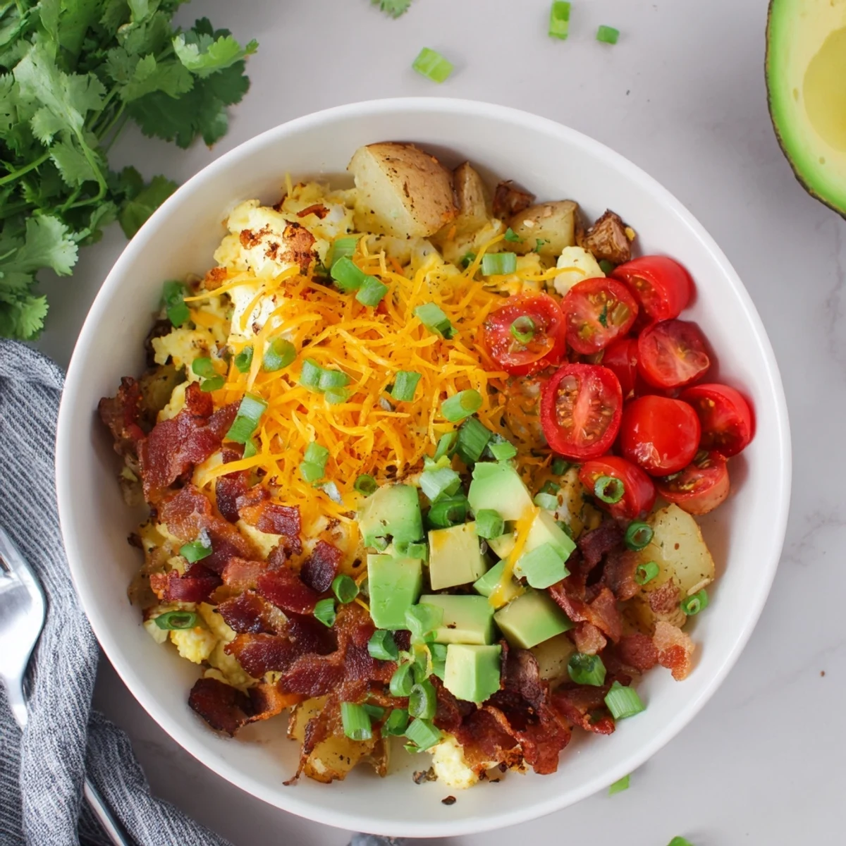 A close-up of a Loaded Breakfast Bowl with fluffy scrambled eggs, crispy roasted potatoes, and crumbled bacon topped with melted cheese.