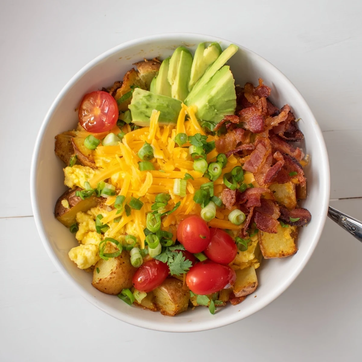 Loaded Breakfast Bowl features a fork lifting cheesy eggs and potatoes, served with hot sauce for a savory morning meal.