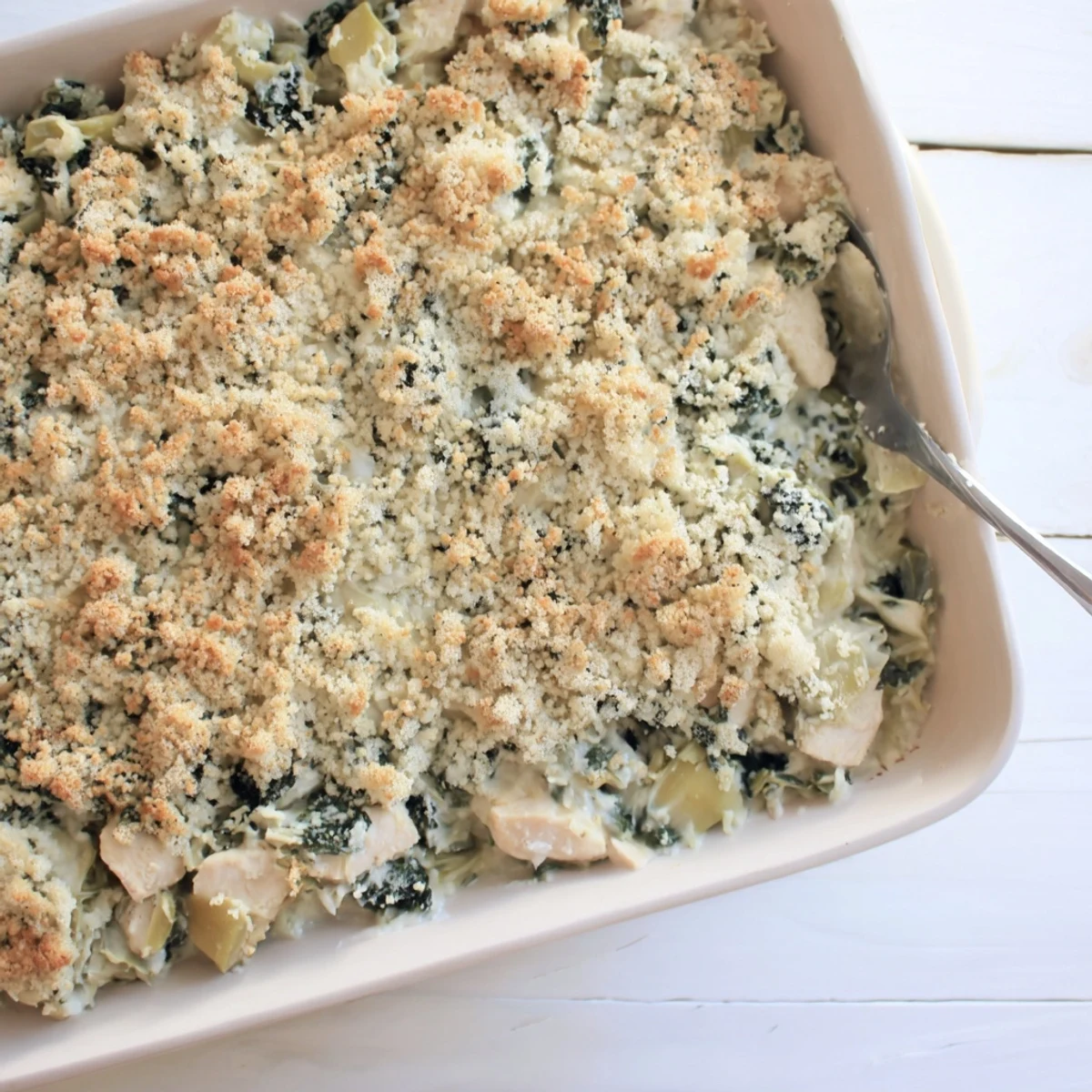 Creamy baked casserole dish featuring tender chicken, spinach, and artichokes under crispy breadcrumbs