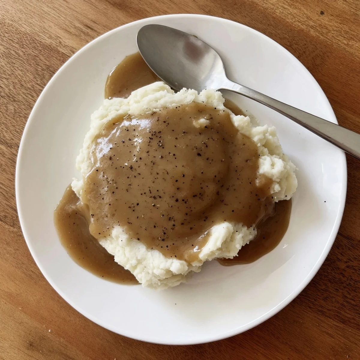 Golden homemade gravy poured generously over fluffy mashed potatoes in a white serving bowl