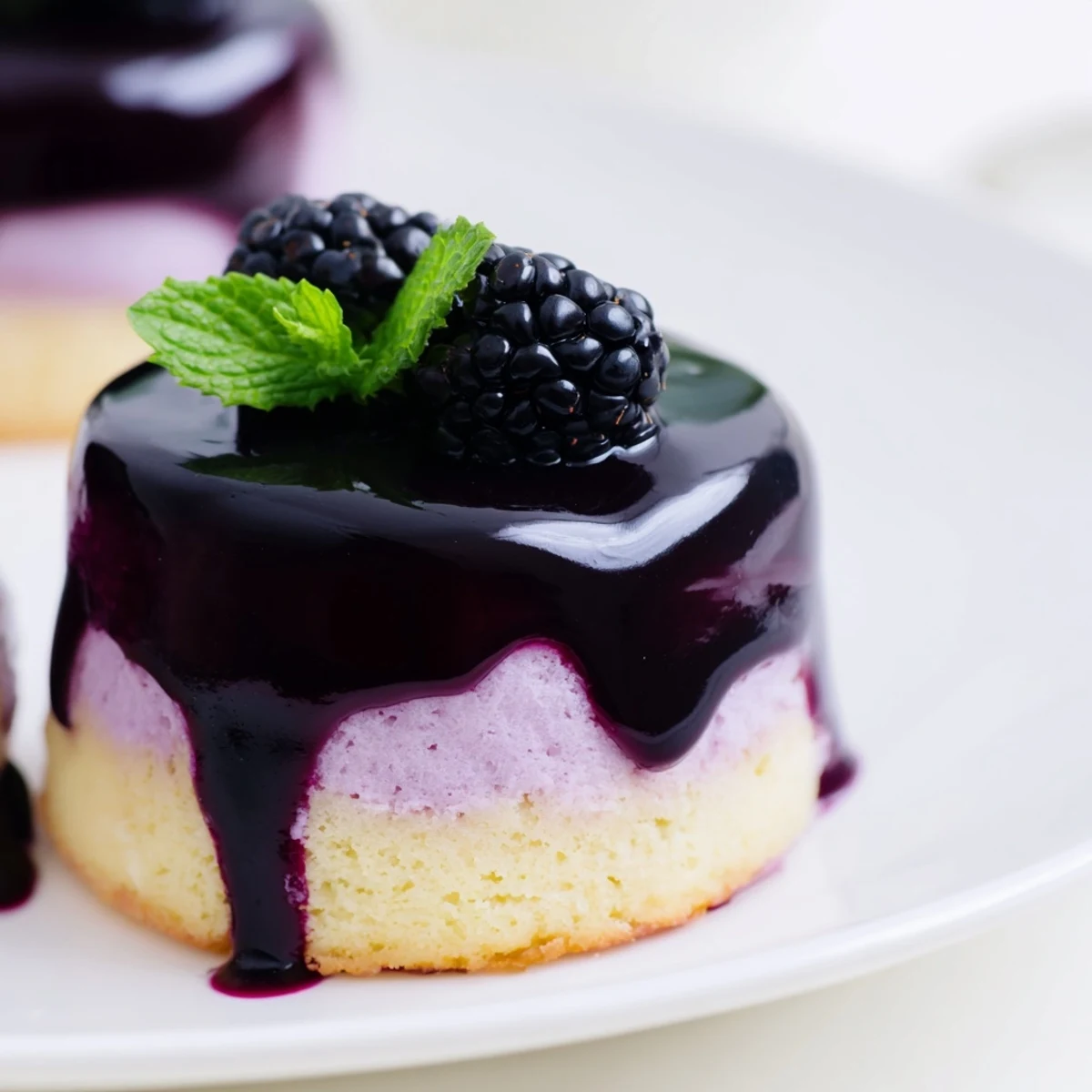 Mini blackberry mousse cakes topped with glossy purple glaze and fresh berries