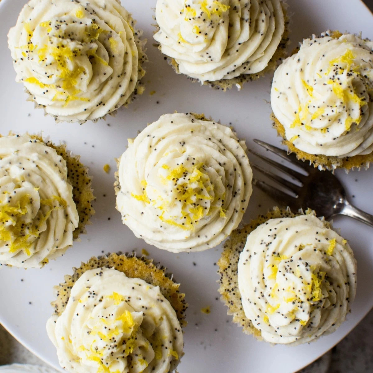 Golden lemon poppy seed cupcakes topped with swirls of creamy lemon frosting and fresh zest
