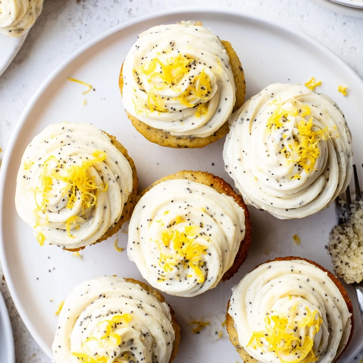 Freshly baked lemon poppy seed cupcakes cooling on rack with generous fluffy lemon frosting