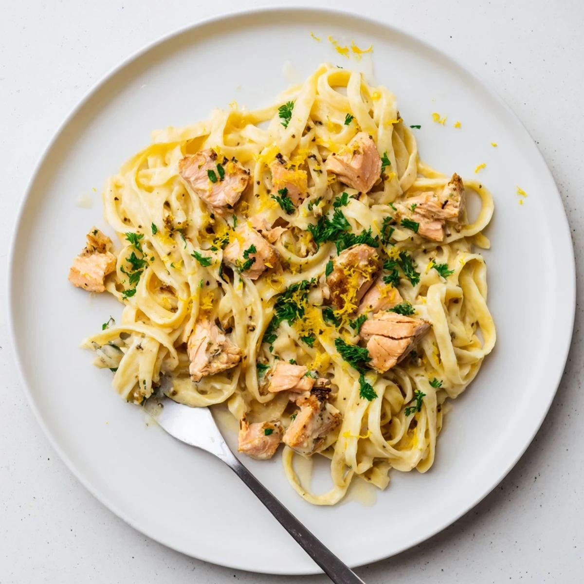 White plate featuring garlic butter salmon fettuccine pasta dish with lemon wedge and chopped parsley