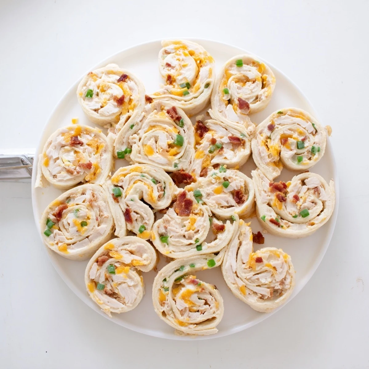Golden spiral pinwheels filled with creamy chicken, cheese, and crispy bacon on a white serving platter