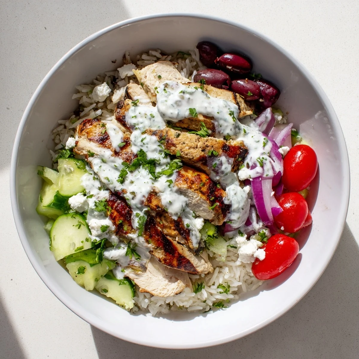 Hearty Greek chicken bowls arranged over steaming rice with colorful cherry tomatoes, Kalamata olives, and cool yogurt dressing