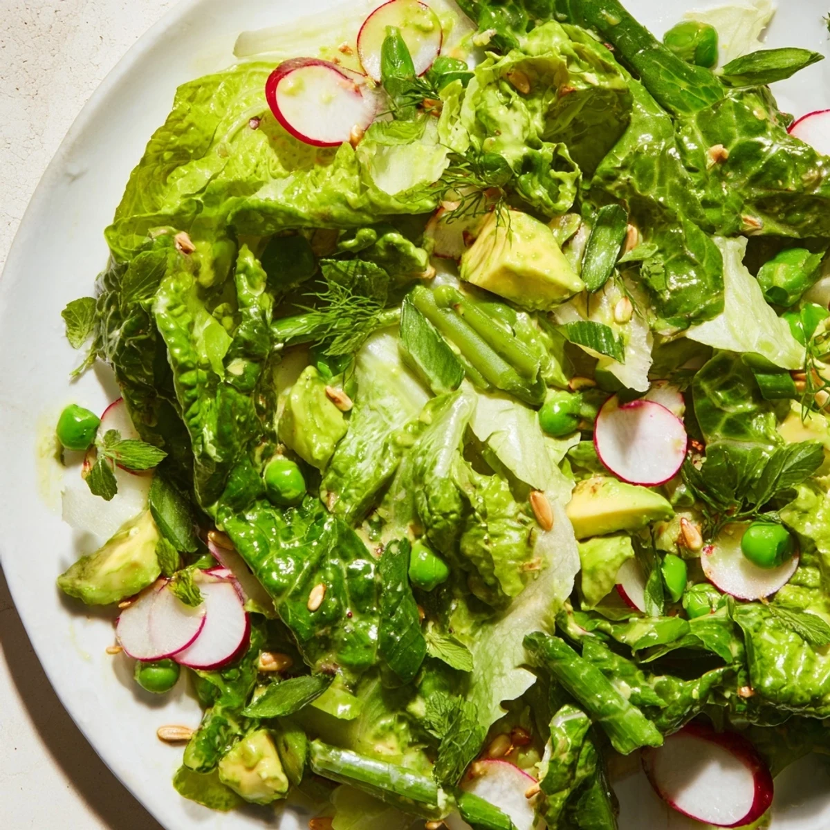 Fresh Green Goddess Salad bowl with crisp vegetables, avocado, and creamy homemade green dressing drizzled over mixed greens
