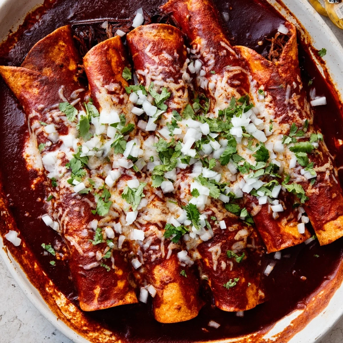 Baked birria enchiladas smothered in rich consommé with Oaxaca cheese, diced onion, and lime wedges