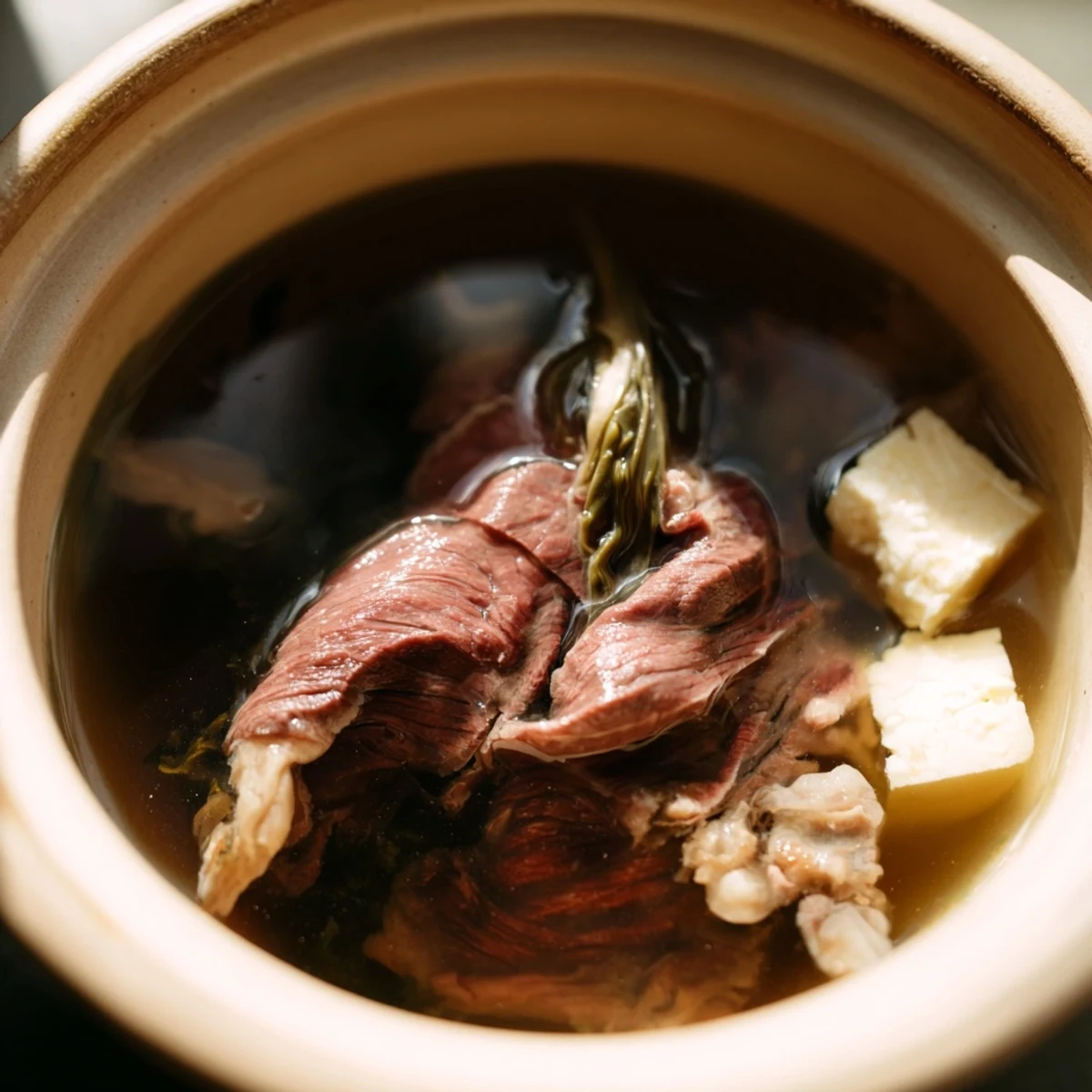 Golden broth steams in a traditional pot surrounded by platters of thinly sliced beef and fresh vegetables for Japanese Shabu Shabu hot pot