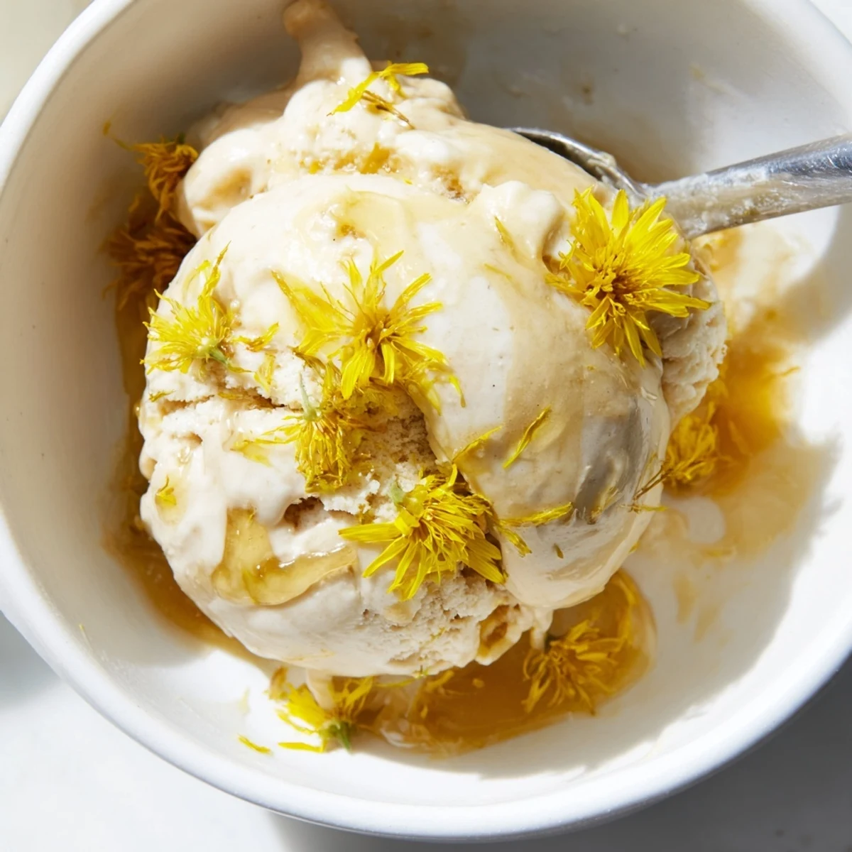 Creamy dandelion honey ice cream scooped into bowls topped with golden petals