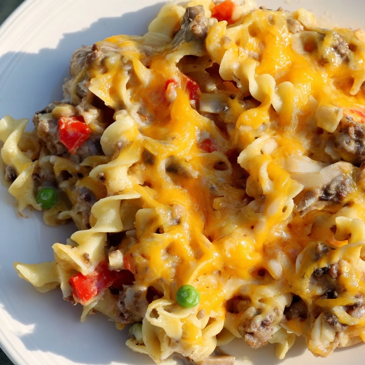 Creamy Cheesy Beef and Noodle Casserole topped with melted cheddar in a glass baking dish