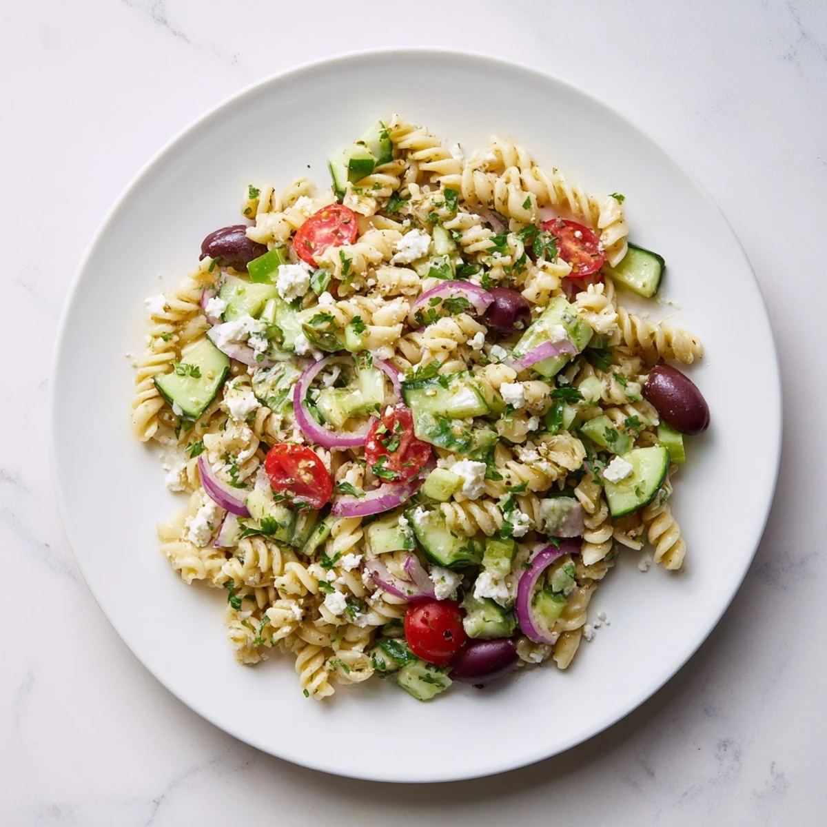 Greek pasta salad loaded with crisp cucumbers, cherry tomatoes, and creamy feta in a zesty herb dressing