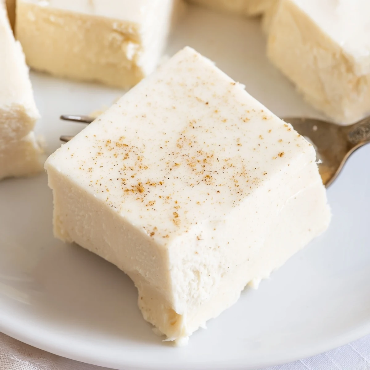 Creamy Eggnog Fudge squares dusted with nutmeg on parchment, holiday ready.