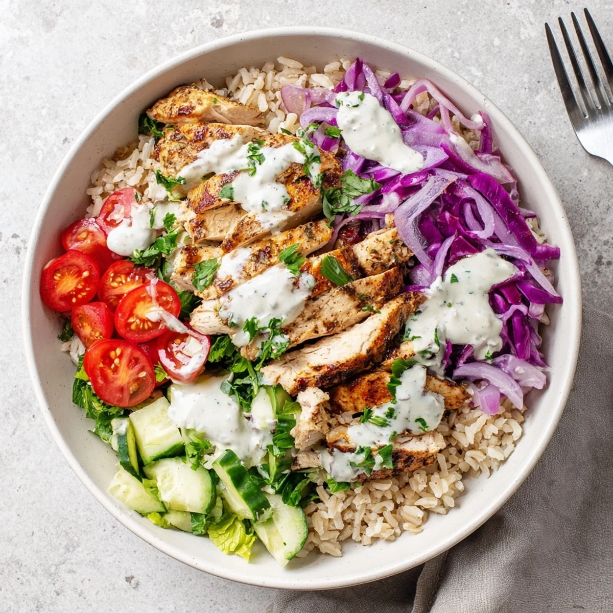 Golden marinated chicken slices arranged over a bed of crisp vegetables and drizzled with creamy tahini yogurt sauce in this healthy chicken shawarma bowl