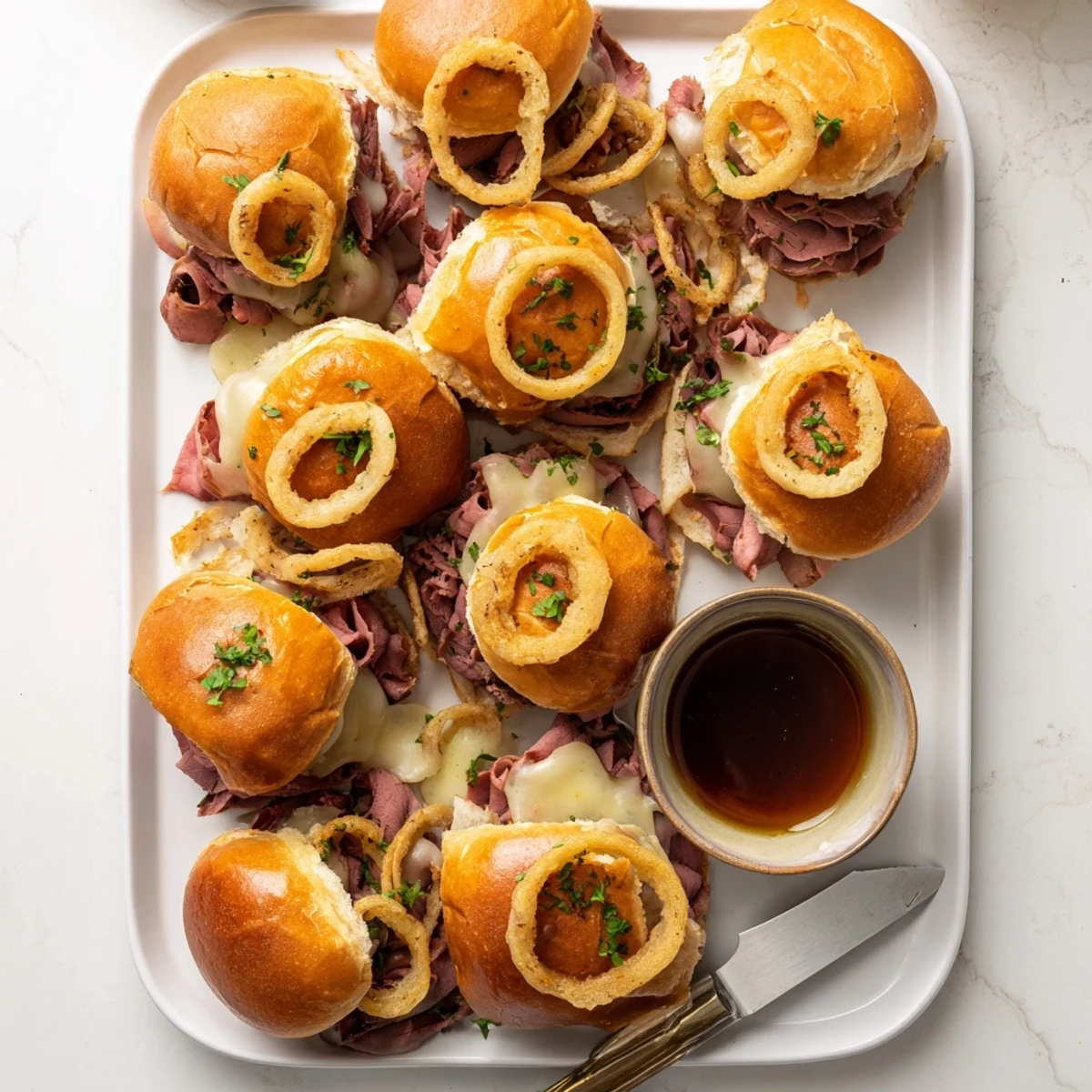 Soft slider rolls piled high with roast beef and onions for French dip sliders