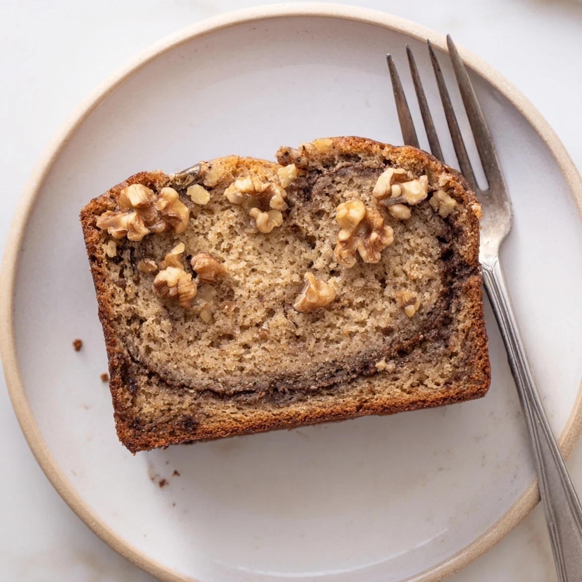 Warm banana nut bread with cinnamon swirl served on wooden cutting board with walnuts