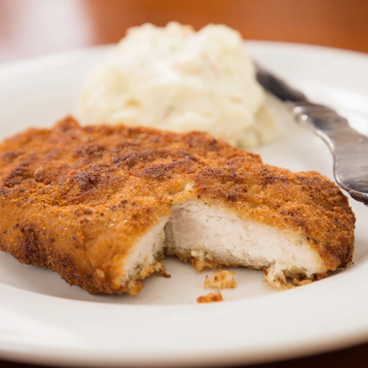 Skillet sizzling, Fried Chicken Breast glistens with oil on paper towels.