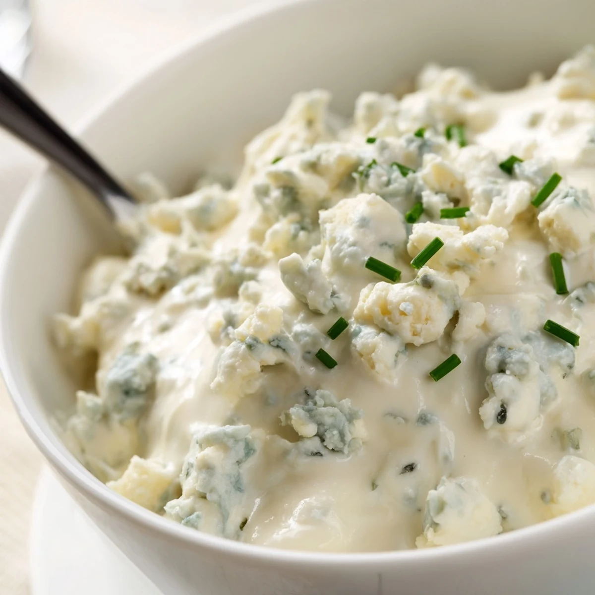Cool blue cheese dip swirled in a white bowl with chunks of tangy crumbled cheese