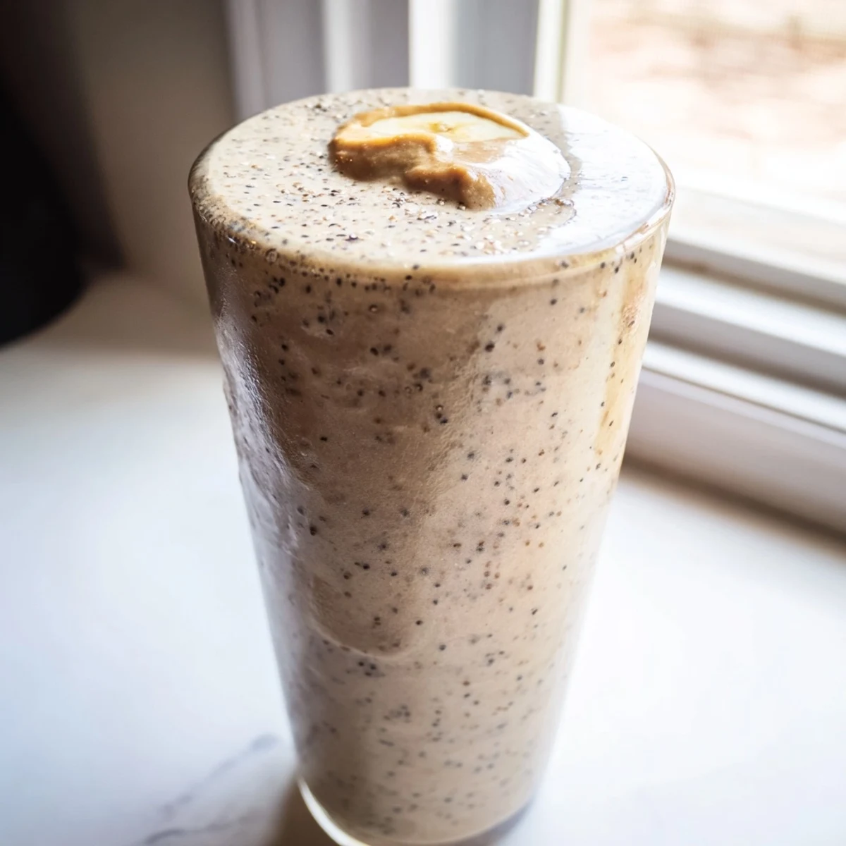 Creamy banana protein coffee smoothie poured into a glass with cinnamon dusted on top